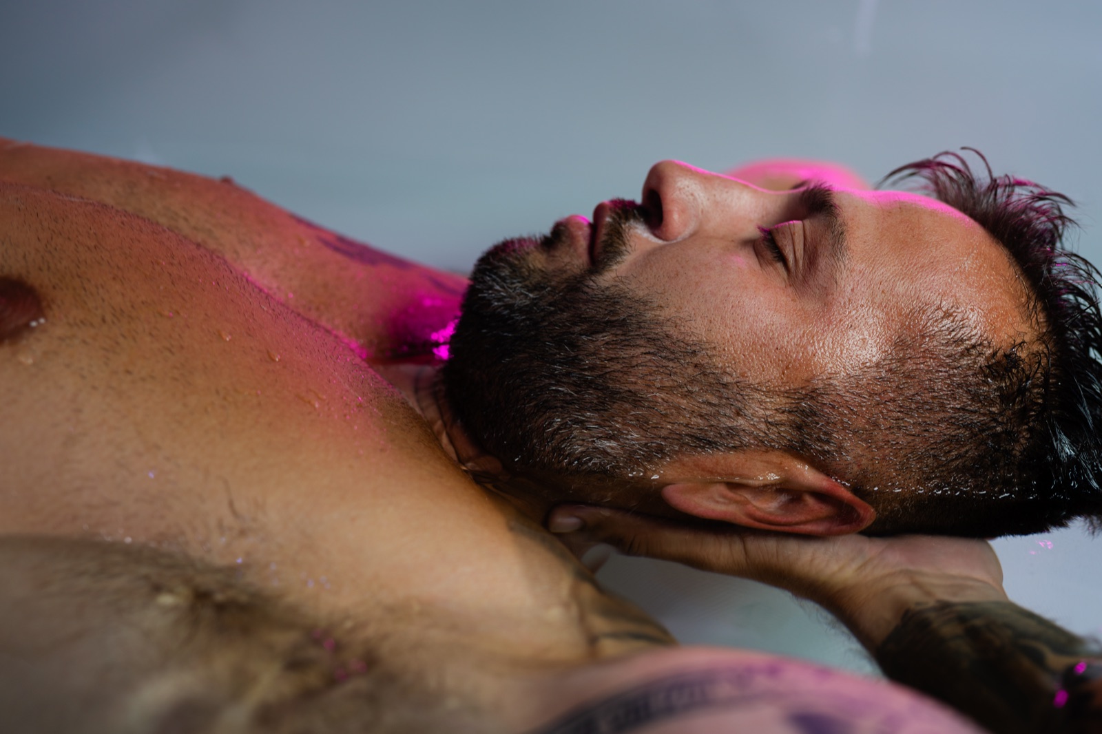 FLOAT ONE guest resting with his eyes closed under soft magenta light