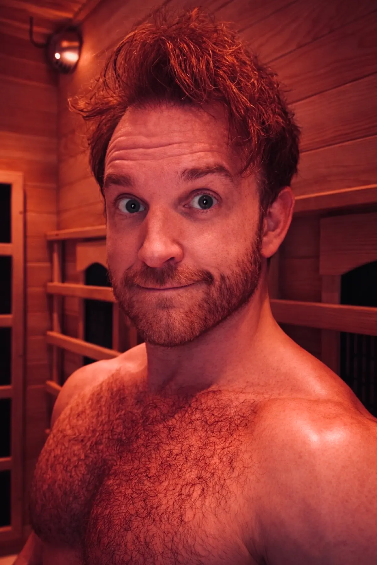 Guest seated in FLOAT ONE's timber infrared sauna under warm red light